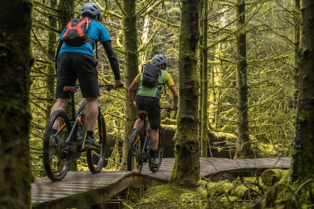 Dos ciclistas con mochilas y cascos duranle su experiencia de ciclismo de cerro en el bosque 