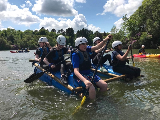  Grupo de 6 amigos con ayudas de flotabilidad azules y cascos blancos haciendo sentadillas- top-paddleboarding