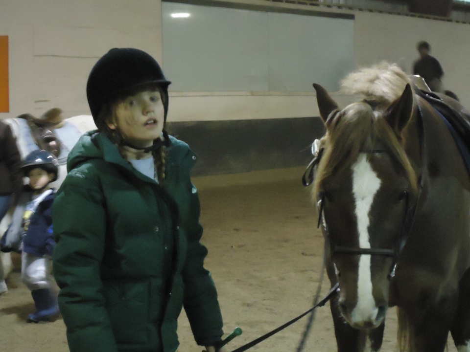  Niña con casco negro, suéter verde y a punto de subir a caballo 