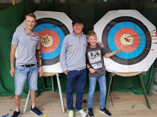 Padre e hijo sonriendo al lado de su instructor duranle su sesión de jalo con arco