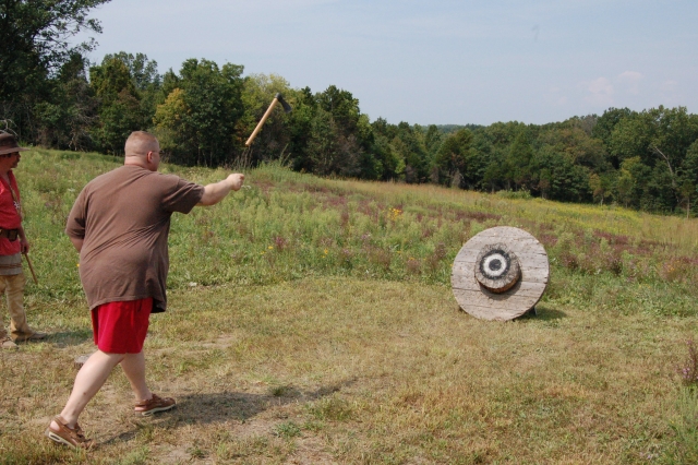  Hombre con playera beige y pantalón rojo aventando hachas