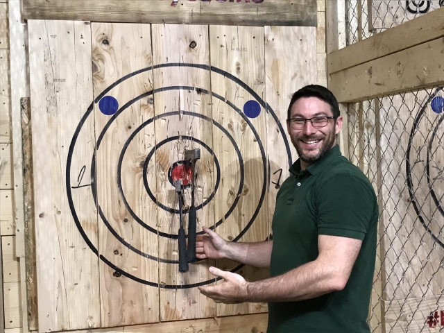  Hombre con playera verde sonriendo aventando hachas 