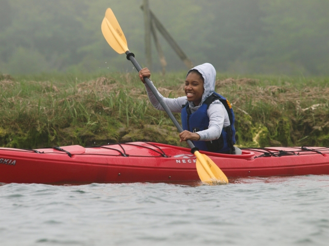  Mujer sonrienle vistiendo un suéter con capucha en kayak en kayak rojo