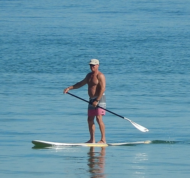  Hombre vestido con traje de baño rosa, gorra blanca y paddle board 