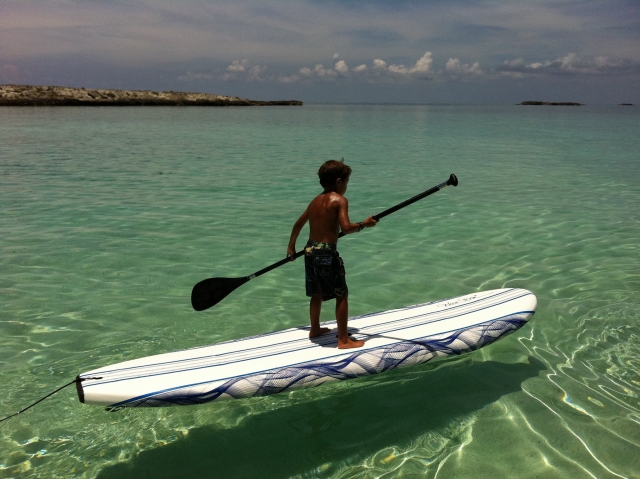  Niño con un maravilloso bronceado practicando paddle board sobre una tabla blanca 