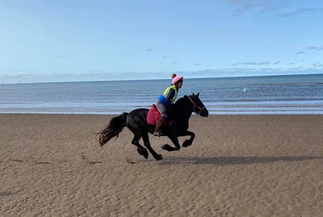  Mujer con sombrero rosa y botas altas cabalgando por la playa 