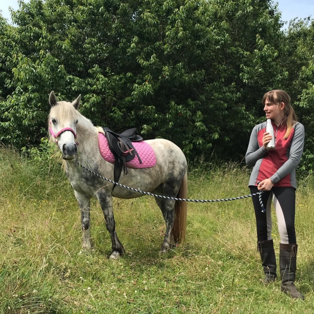  Chica sonriendo a punto de tener su lección privada con un caballo blanco 