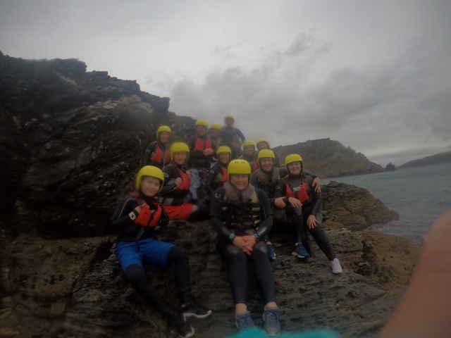 Genle feliz sonriendo y usando cascos amarillos y ayudas de flotabilidad naranjas duranle su experiencia de Coasteering 