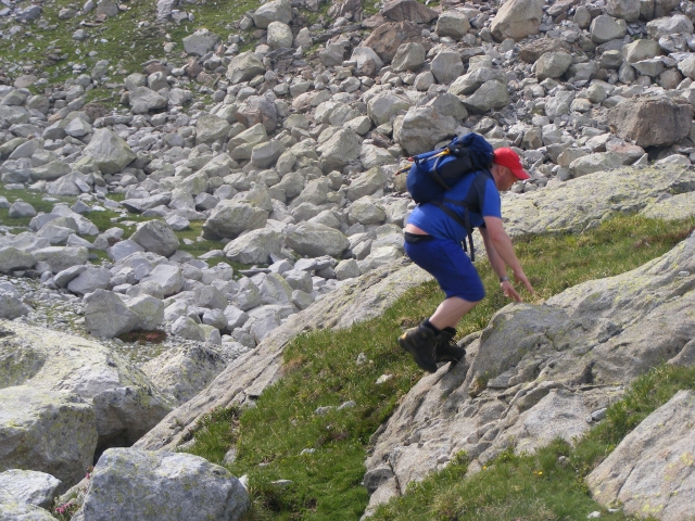  Hombre con pantalones cortos y playera azules, gorra roja y mochila escalando 