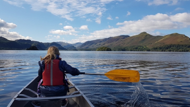 Chica con ayudas de flotabilidad rojas navegando en canoa y montañas frenle a ella 