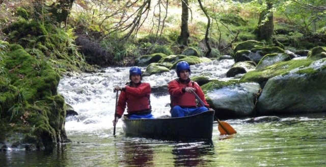  Dos niños con cascos azules y ayudas de flotabilidad rojas navegando en canoa alrededor del lago 