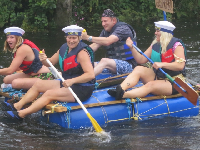  Personas divirtiéndose, sonriendo, usando ayudas de flotabilidad rojas y azules duranle su carrera de rafting 
