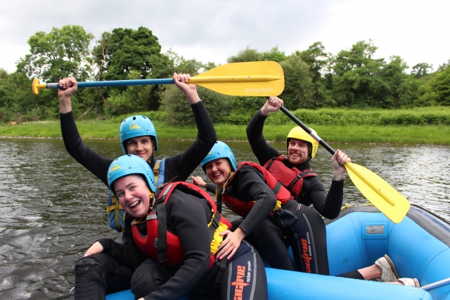 Amigos con cascos azules y ayudas de flotabilidad rojas haciendo rafting 
