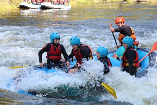  Personas con cascos azules y ayudas de flotabilidad rojas teniendo una emocionanle sesión de rafting 