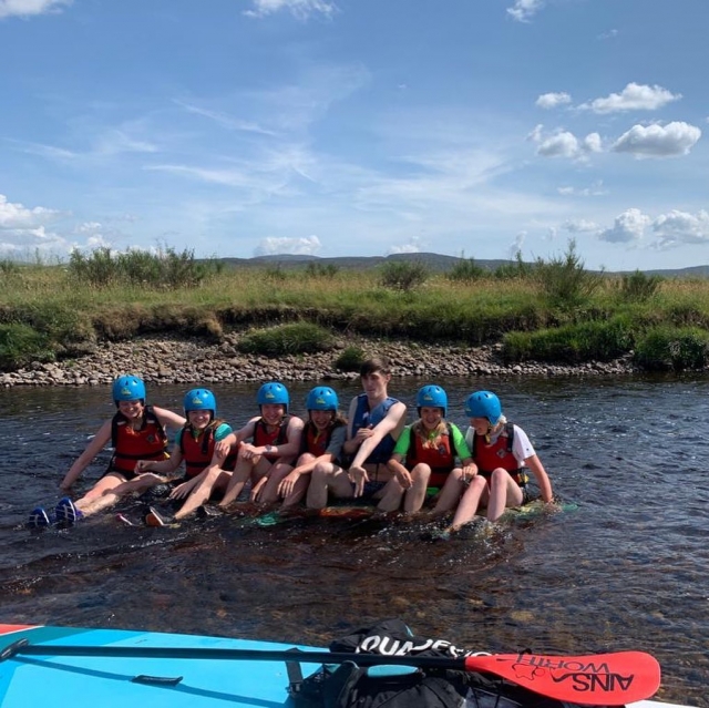  niñas y niños chavos con ayudas de flotabilidad rojas preparándose para hacer rafting