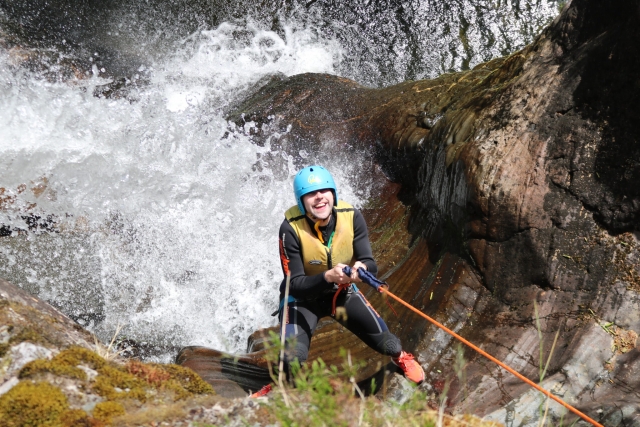  Niño sonriendo, usando casco azul, ayudas de flotabilidad amarillas y escalando