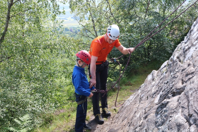 Instructor con playera naranja enseñando a un niño a escalar en roca