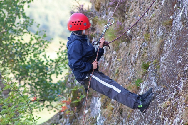 Niño con casco rojo escalando en roca por primera vez