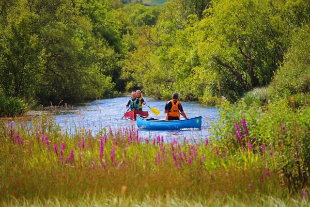 Tres personas divirtiéndose paseando en canoa y usando ayudas de flotabilidad azules y naranjas 