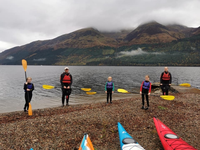  Familia usando ayudas de flotabilidad azules y rojas, sonriendo y preparándose para navegar en kayak 