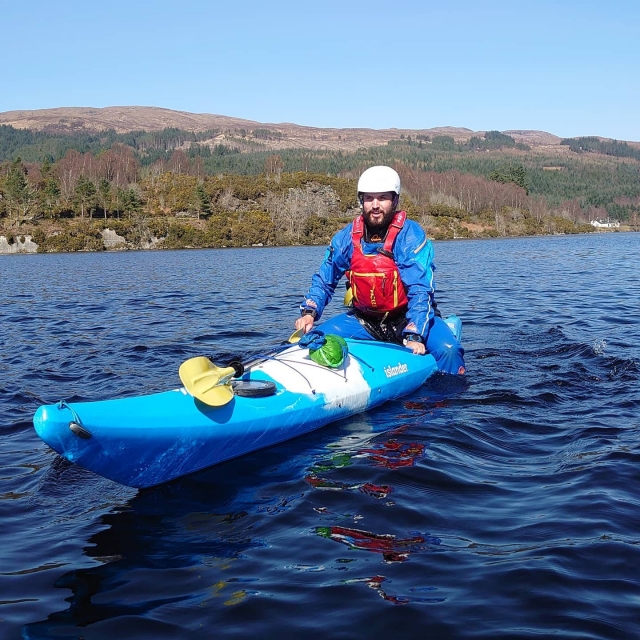  Hombre con casco blanco, ayudas de flotabilidad rojas sonriendo y navegando en kayak 