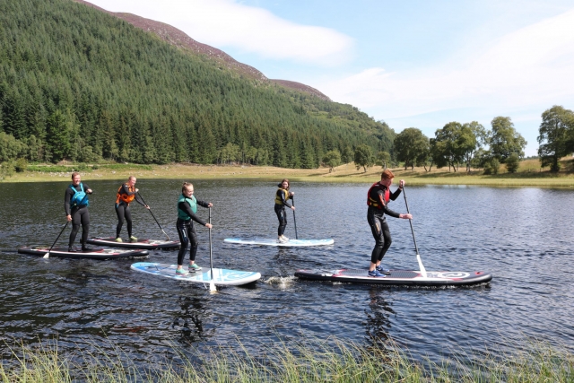 Familia usando ayudas de flotabilidad azules, amarillas y naranjas haciendo paddleboard en el río