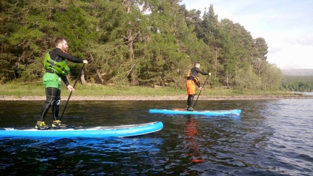 Dos hombres usando ayudas de flotabilidad verdes y naranjas haciendo paddleboard
