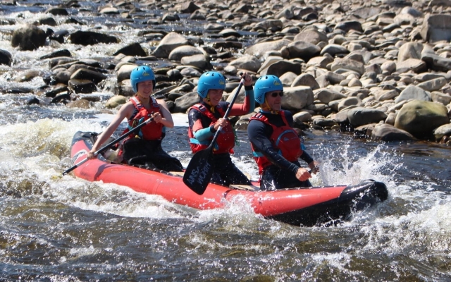  Un hombre y dos mujes con cascos azules y ayudas de flotabilidad rojas haciendo rafting