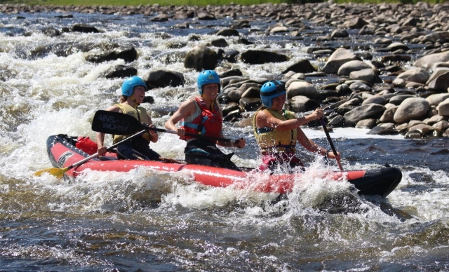  Tres niñas riendo y usando cascos azules y ayudas de flotabilidad rojas y verdes haciendo rafting 