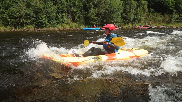  Niño con casco rojo y ayudas de flotabilidad azul haciendo kayak 