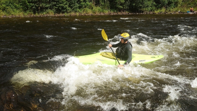  Niño con casco amarillo y traje de neopreno negro haciendo kayak