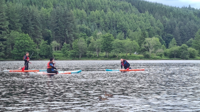 Tres personas con ayudas de flotabilidad rojas haciendo paddleboard 
