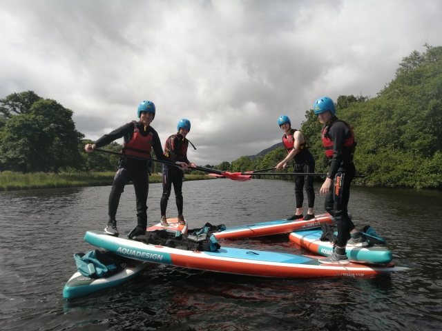  Dos parejas de amigos con cascos azules y ayudas de flotabilidad rojas preparándose para hacer paddleboard