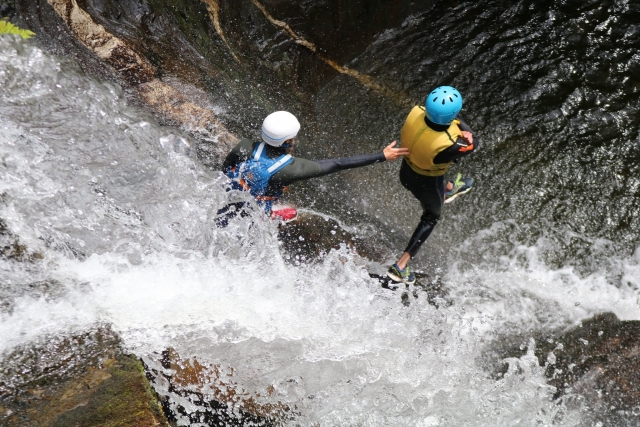  Aventurero con casco azul y ayudas de flotabilidad amarillas saltando con la ayuda de un instructor 
