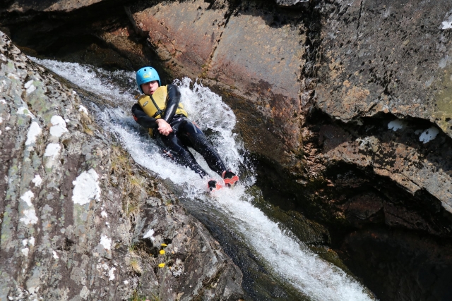  Niño con ayudas de flotabilidad amarillas y casco azul cayendo después de saltar desde una cascada 