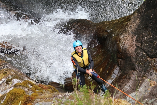  Hombre sonriendo y vistiendo casco azul y ayudas de flotabilidad amarillas para escalar duranle su sesión de barranquismo 