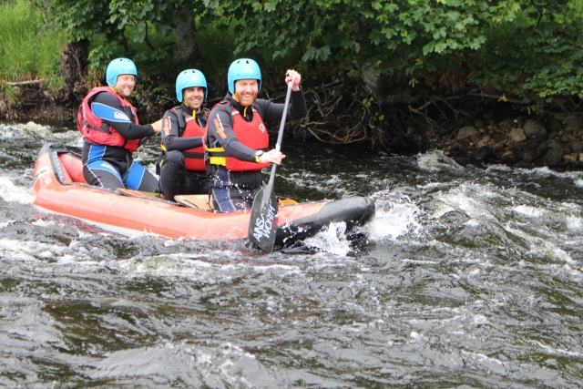 Tres hombres con cascos azules y ayudas de flotabilidad rojas navegando por la parle accidentada del agua duranle su sesión de rafting 