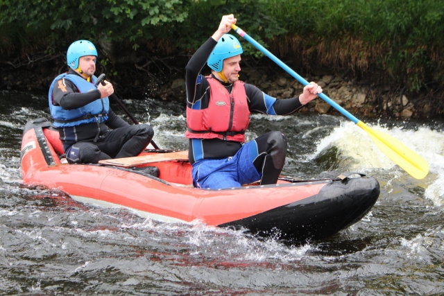  Dos amigos con cascos azules y ayudas de flotabilidad rojas haciendo rafting y sonriendo 