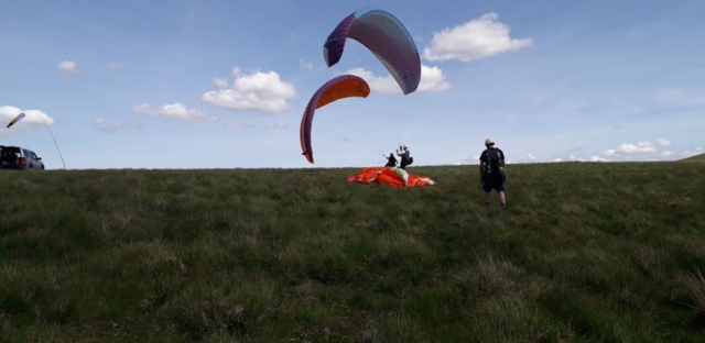 Dos personas a punto de hacer parapenle usando parapentes azules y naranjas 