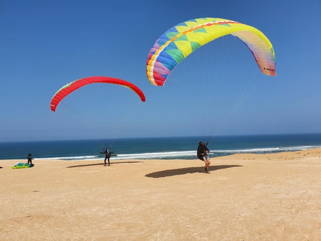 Tres personas aterrizando en la playa después de un parapenle Sesión con parapenle amarillo y rojo.