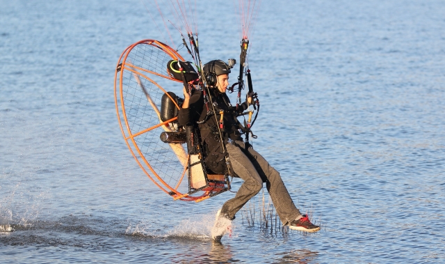  Chica con casco negro y suéter tocando el agua duranle su sesión de paramotor