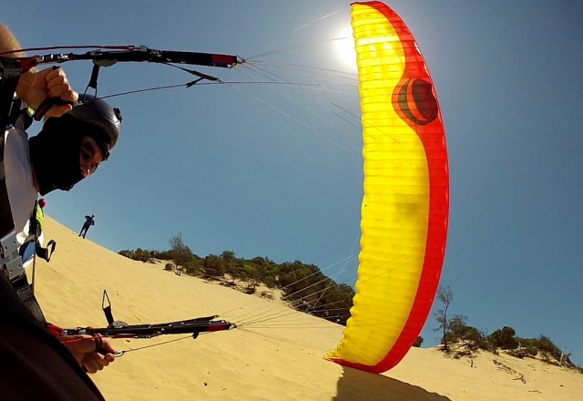  Paramotor amarillo y rojo utilizado por un hombre con casco negro y despegando de la playa 