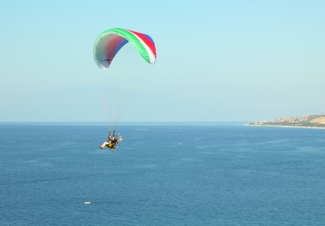  Paramotor de colores llevando a un aventurero en el aire y volando sobre la playa 