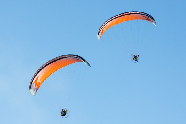 Dos personas disfrutando de su experiencia en paramotor, volando con paramotores naranjas 