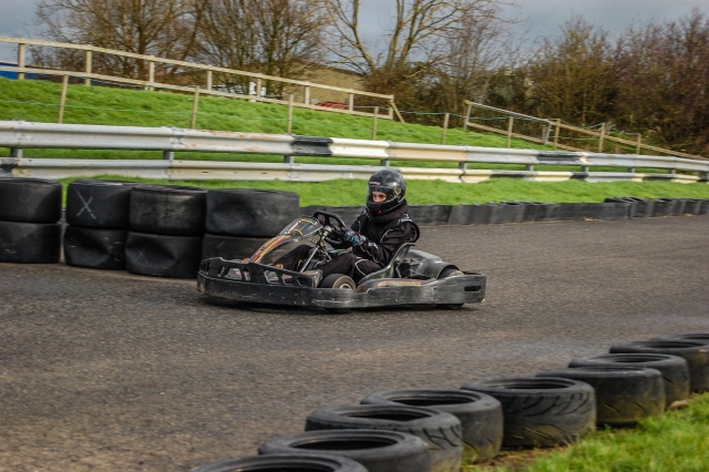 Niño vestido con traje de manejar negro y casco divirtiéndose con su recorrido de karting 