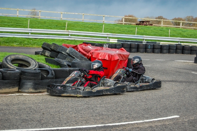  Dos personas, una con traje de manejar rojo y casco negro y la otra, casco negro y traje de conducción, karting 