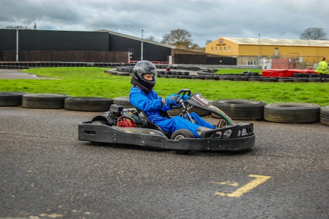 Niño con traje de manejar azul y casco negro karting con neumáticos a lo largo de la pista 