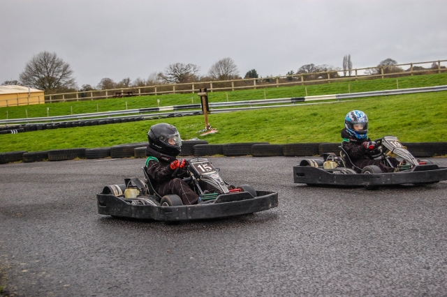  Dos chavos, uno con casco azul y otro negro, y ambos con trajes de conducción negros duranle su carrera de karting 