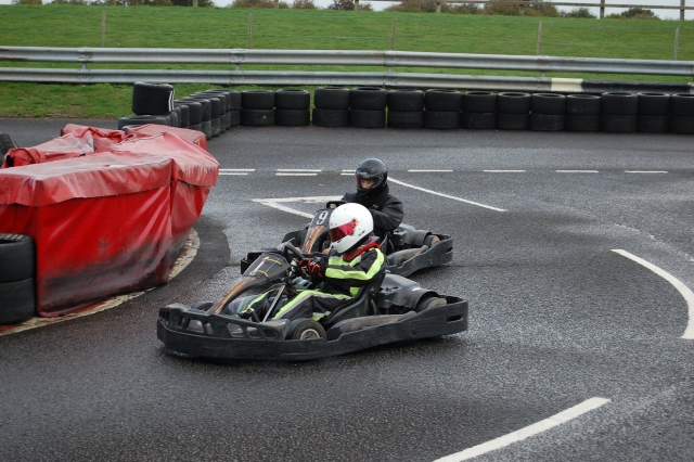  Conductor con traje de conducción verde y negro y casco negro y otro conductor con casco y traje de conducción, todos de negro, duranle su Carrera de Karting Grand Prix 