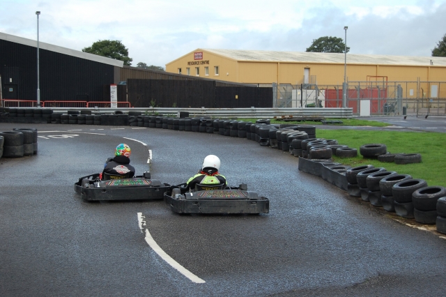 Dos karts y dos conductores con cascos blancos y negros y trajes de conducción negros vistos desde atrás duranle su carrera de karting 